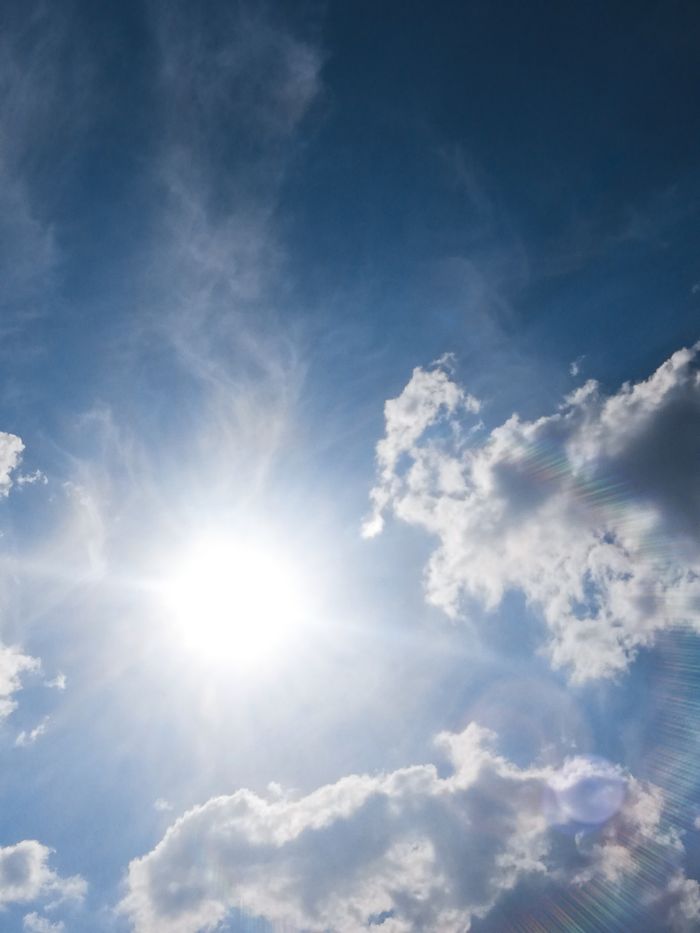 A radiant sun shining through fluffy clouds in a vibrant blue sky.